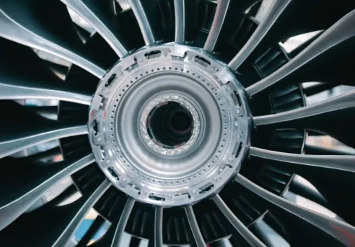 High-detail close-up photograph of a large jet turbofan engine’s polished metallic front fan blades and central rotor hub, aerospace heavy industry mechanical component texture