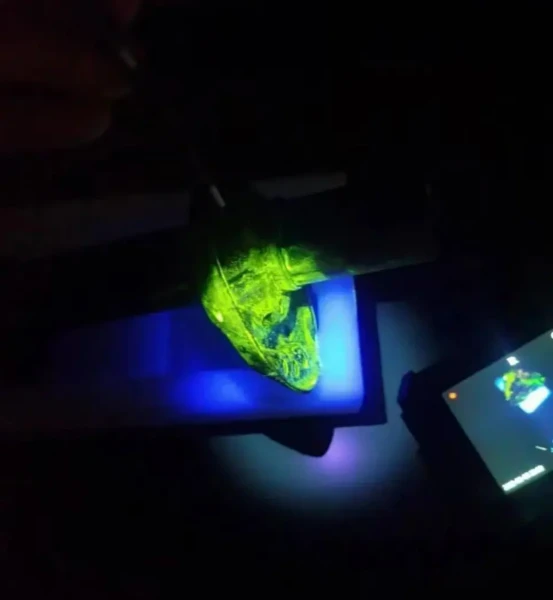 Dark field field test shot, UV borescope illuminates mechanical workpiece; fluorescent penetrant gathers inside surface flaws and emits bright yellow-green fluorescence under 365nm ultraviolet excitation
