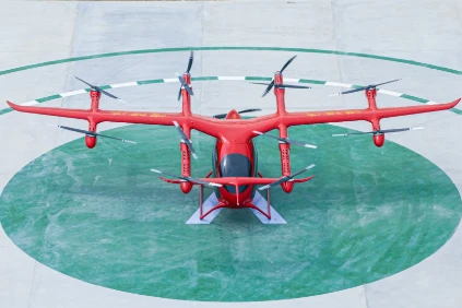 Bright red electric vertical takeoff and landing passenger aircraft with 12 rotors, stationary on marked green helipad for urban air mobility transportation