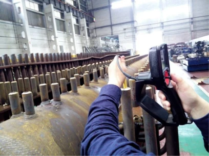 Industrial worker using handheld video borescope to inspect large heat exchanger tube bundle in factory workshop