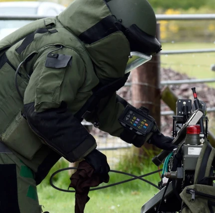 Bomb disposal expert in EOD suit operating inspection robot in field environment