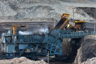 Open‑pit coal mine, heavy‑duty dump truck unloading ore into mobile crushing plant, dust suppression spray working in mining site