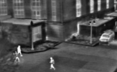 Grayscale thermal imaging screenshot showing pedestrians and buildings in nighttime urban scene
