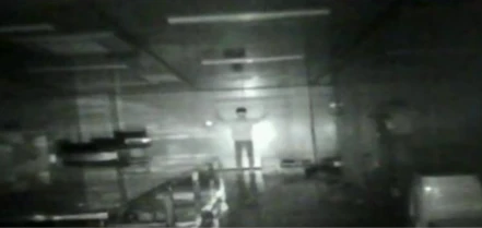 Low‑light grayscale image captured by infrared inspection camera, human figure in dark indoor warehouse